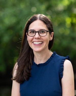 professor in a blue shirt in front of a forested backdrop